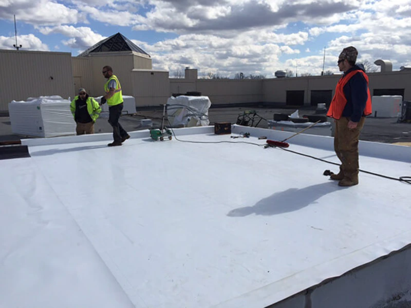 Roofing crew installing a white TPO roofing membrane on a commercial flat roof building in the Muskoka area.
