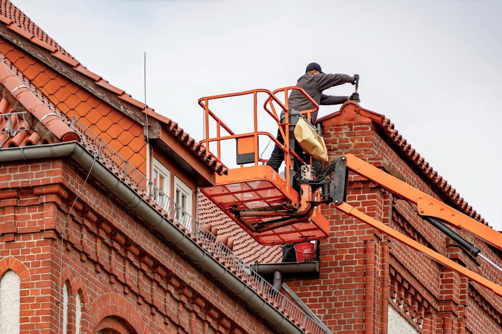 Flat Roofing in Muskoka 5 Roofer in a cherry picker conducting maintenance on a red brick building with a tiled roof.