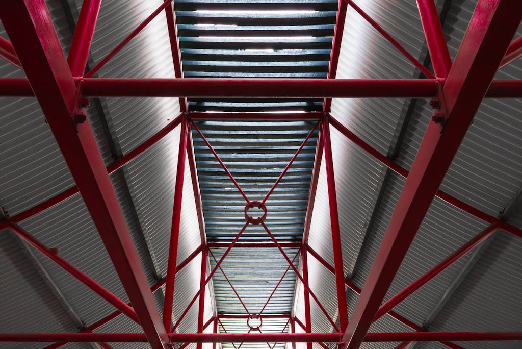 View of a steel roof supported by red beams in an industrial setting, emphasizing structure.